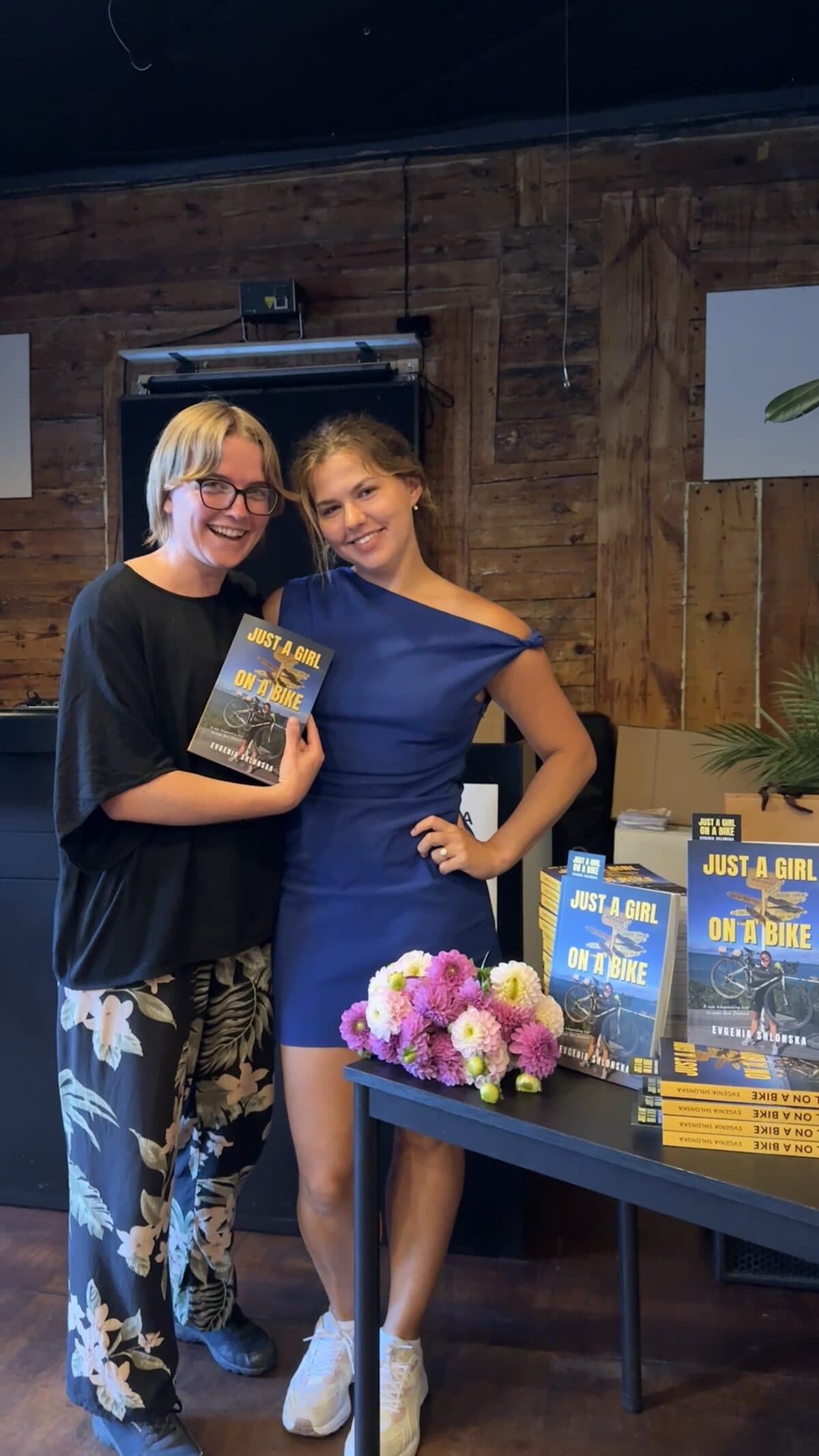 Evgenia and a guest holding a copy of the book, with stacks of copies on the table
